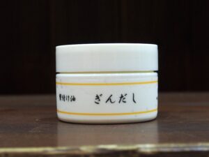 ぎんだし／鬢付け油は、天然保湿成分が豊富な植物オイル100％で、形状は、固形状のオイルです。ハゼやウルシから採れる木蝋(モクロウ)をベースに、椿油などの植物油で作られていて、つやのあるまとめ髪やスタイリングを楽しむことができます。