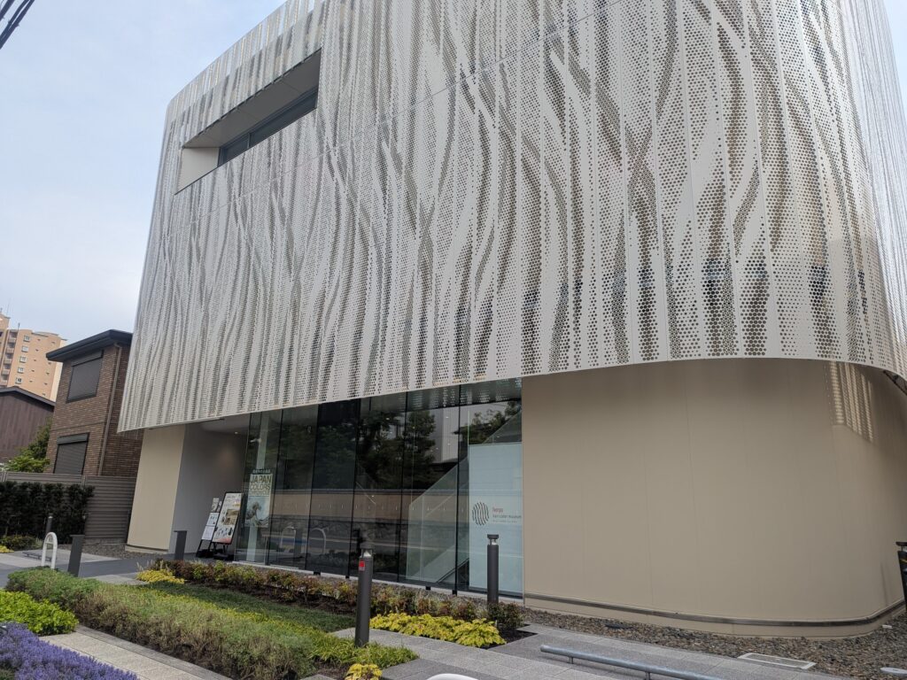 Curved contemporary building with a perforated metal facade, glass storefront, and landscaped foreground.